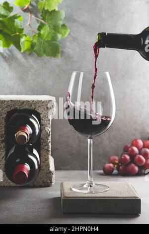 Bottle of red wine poured into the wine glass on concrete background. Vertical format. Beverage and wine concept. Stock Photo