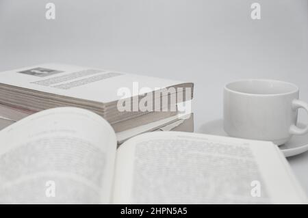 Image of a table on which there is an open book with the text blurred, a stack of books and a cup of coffee on a white background and copy space Stock Photo