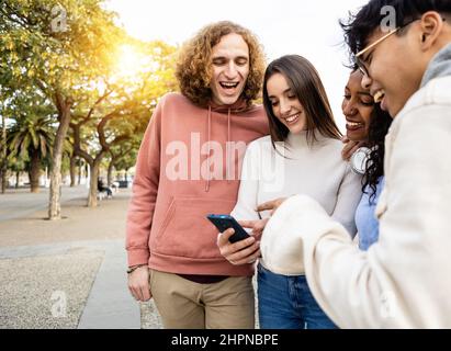 Happy diverse friends laughing while watching funny videos on smartphone Stock Photo