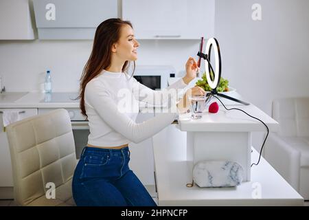 Beauty blogger uses ring light with cell phone holder during live stream at home. Stock Photo