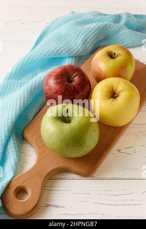 A group of four colored apples on a wooden board and a blue napkin on a white wooden background. Stock Photo