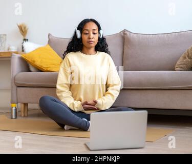 African-american female listening to music in headphones while meditating with laptop at home Stock Photo