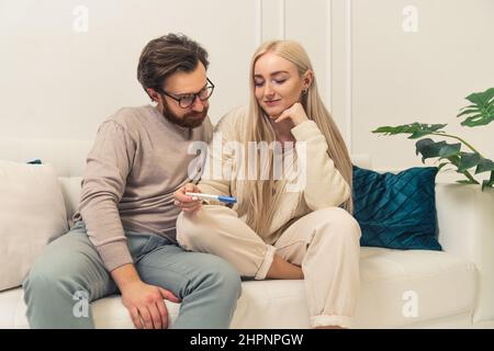 caucasian businessman finds out that his blonde long-haired fiancee is pregnant by looking at a pregnancy test results. High quality photo Stock Photo