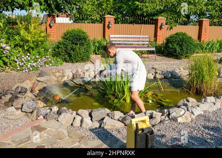 Man cleans garden pond bottom with high-pressure washer from mud and sludge. Stock Photo