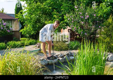 man cleans garden pond bottom with high-pressure washer from mud and sludge. Stock Photo