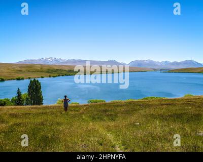 A female tourists stops to enjoy the scenic view towards the mountains above Lake Alexandrina, in Canterbury, New Zealand Stock Photo