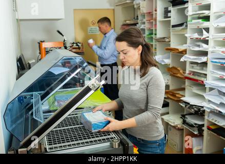 Female worker packs notebooks in a vacuum packing Stock Photo