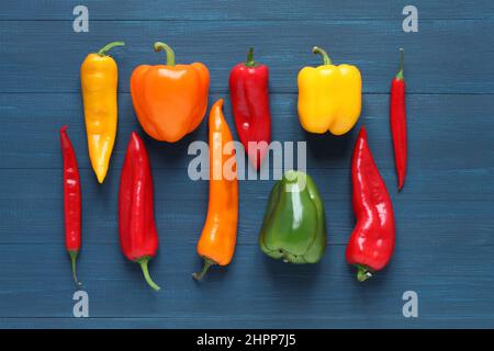 Multicolored sweet bell peppers, cappi peppers and hot chili peppers on a blue wooden table. View from above. Closeup. Stock Photo