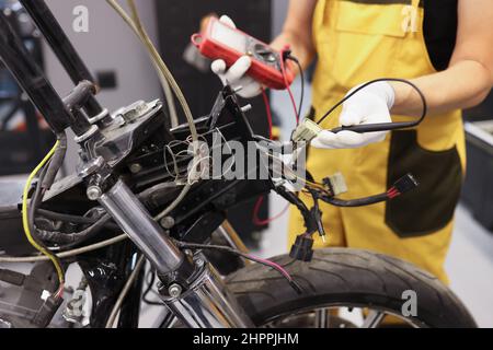 Mechanic using multimeter checks voltage level motorcycle battery motorcycle garage Stock Photo