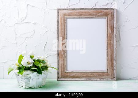 Wooden picture frame mockup with apple blossom in the white wicker basket. Empty frame mock up for presentation design. Template framing for modern ar Stock Photo