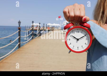 Alarm clock for ten in morning in female hand against backdrop of sea. Sundial on sea concept Stock Photo
