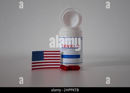 Covid19 pill bottle with several pills outside the bottle and a US flag on a lab bench Stock Photo