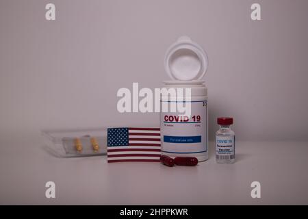 Covid19 pill bottle with several pills outside the bottle and a US flag on a lab bench Stock Photo