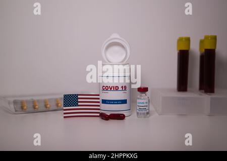 Covid19 pill bottle with several pills outside the bottle and a US flag on a lab bench Stock Photo
