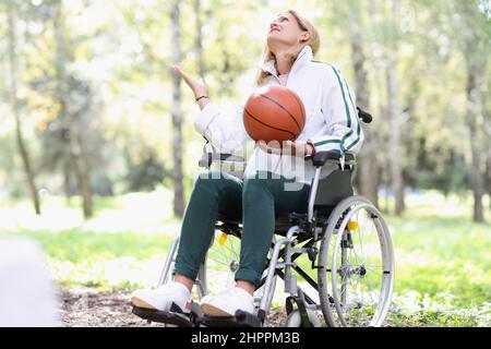 Young woman sitting in wheelchair holding basketball in park Stock Photo
