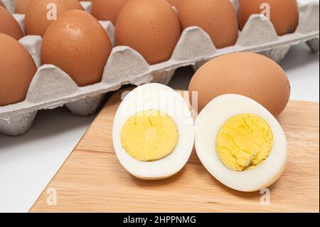 Many eggs and half-cut boiled eggs on wooden chopping board. Stock Photo