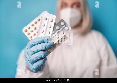 Close up of female doctor looking at camera wearing face mask holding pill blisters antiviral drug against coronavirus covid 19 outbreak