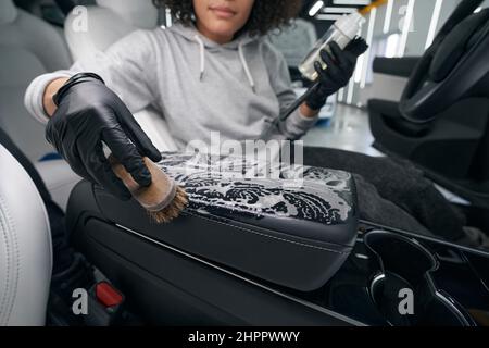 Worker using leather cleaner and brush for cleaning car upholstery Stock Photo
