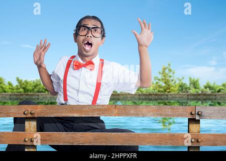 Asian nerd with ugly face falling from wooden fence to the lake Stock Photo