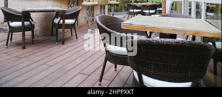 Restaurant terrace rattan bamboo chairs with white cushions and square wooden tables on artificial panel floor Stock Photo