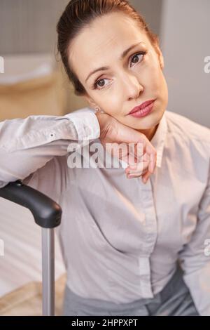 Low-spirited thoughtful woman with baggage sitting alone in hotel room Stock Photo