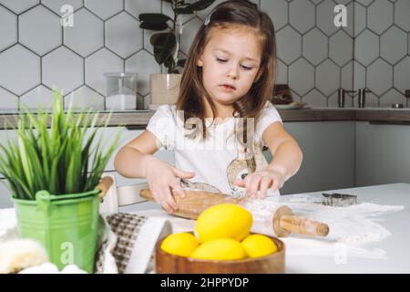 Portrait of little serious girl, helping, learning rolling dough, making shape easter cookies. Sculpt flour biscuit. Preparing holding rolling pin. Ye Stock Photo