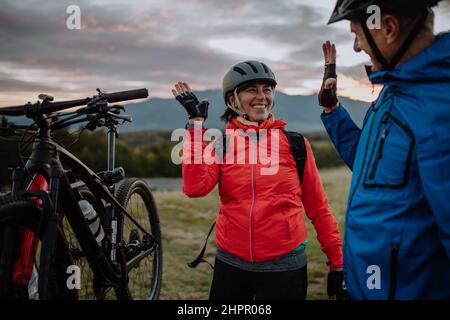 Senior couple bikers high fiving outdoors in forest in autumn day. Stock Photo