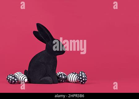 Black and white easter eggs with hearts and stripes next to bunny figure on pink background Stock Photo