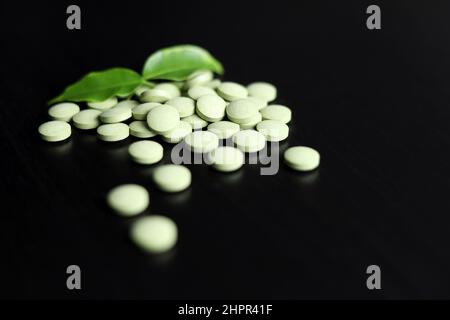 Green pills with leaves scattered on a dark wooden table. Herbal medicines, superfood for health Stock Photo