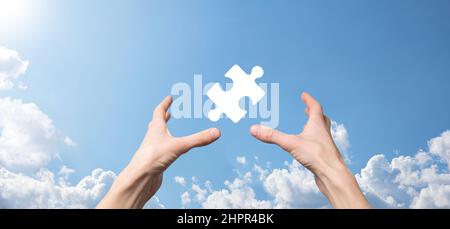 Male hand holding puzzle icon on blue background. pieces representing the merging of two companies or joint venture, partnership, Mergers and acquisit Stock Photo