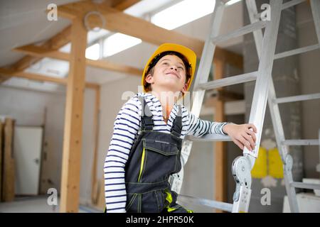 cool young boy with yellow safety helmet posing and having fun on construction building site indoor in a loft Stock Photo