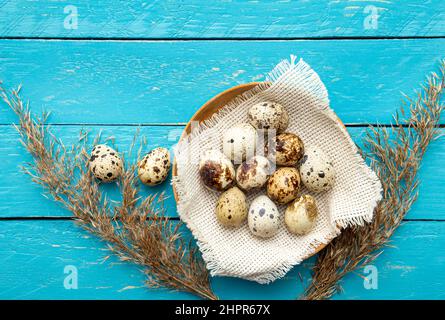 Pile of Quail eggs in natural color wood bowl indoors on blue wooden board background. Flat lay view, lot of copy space. Healthy food concept. Stock Photo
