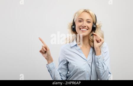 Happy young female call center operator wearing headset and pointing aside at free space, light background, panorama Stock Photo