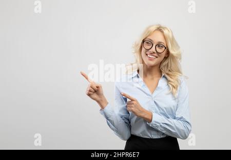 Happy lady entrepreneur in formal wear pointing aside at empty space and smiling at camera, showing cool offer ad Stock Photo