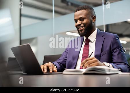 Smiling african american businessman using notebook and taking notes Stock Photo