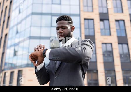 Time management. Focused african american businessman looking at wristwatch, walking during break in downtown area Stock Photo