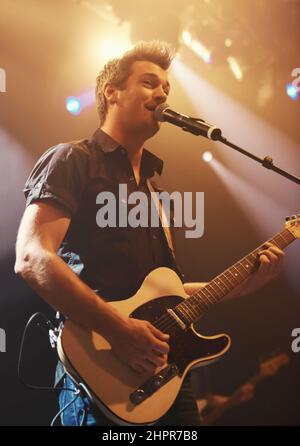A young performer singing and playing his guitar. This concert was created for the sole purpose of this photo shoot, featuring 300 models and 3 live Stock Photo