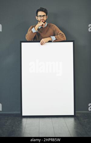Making a big and bold statement. Studio portrait of a young man holding a blank sign against a grey background. Stock Photo
