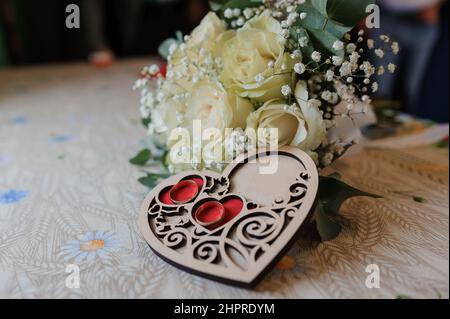Bride's bouquet of white roses, a pair of gold rings on a heart-shaped wooden stand Stock Photo