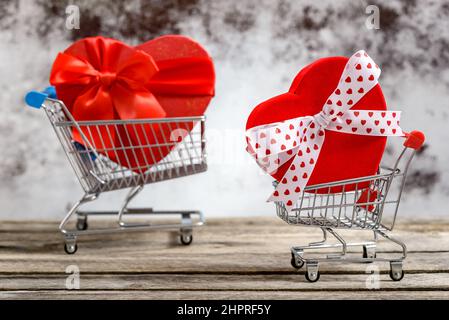 Two shopping carts with gift boxes in heart shape on a rustic wooden table. Sales and shopping concept. Stock Photo