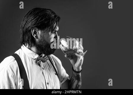 handsome hipster drinking rum glass. party goer with alcohol. brandy or cognac. bearded man in suspenders drink scotch whiskey. brutal guy bartender Stock Photo