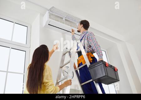 Technician from the repair service fixes the air conditioner in a young woman's home Stock Photo