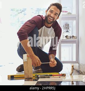 Decorating one tile at a time. Portrait of a smiling man laying floor tiles. Stock Photo