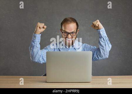 Happy businessman celebrating success and shouting Yes sitting at desk with laptop Stock Photo