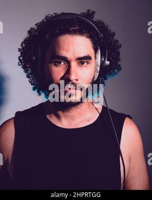 portrait of latin caucasian man with headphones, curlers and beard, in a music studio looking at the camera and smiling. Stock Photo