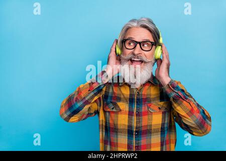 Photo of dreamy man pensioner dressed checkered shirt glasses listening music empty space isolated blue color background Stock Photo