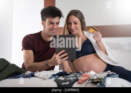 Young pregnant woman with her partner shopping online for the baby with a tablet Stock Photo