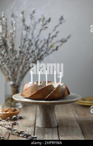 Homemade nuts bundt cake with powder sugar, candles and bouquet of fresh willows on wooden table. Rustic style Stock Photo