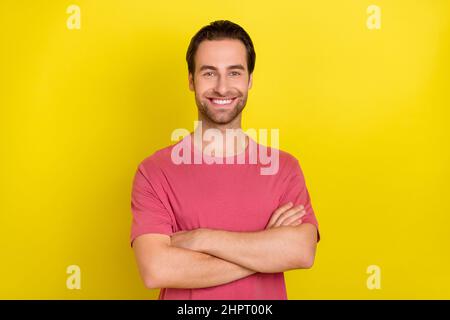 Photo of cheerful self-assured guy folded hands beaming smile wear pink t-shirt isolated yellow color background Stock Photo