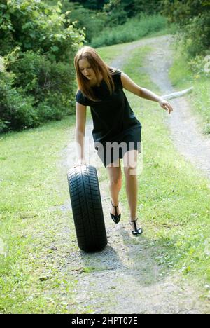 Young woman pushing a car tire down the hill Stock Photo